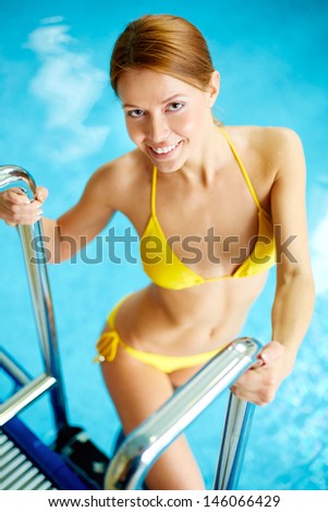 Image of young female in bikini smiling at camera in swimming pool