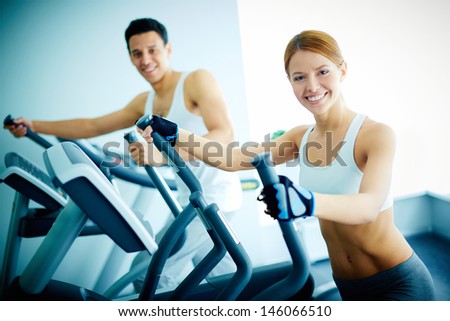 Portrait of pretty girl and young guy training on special sport equipment in gym