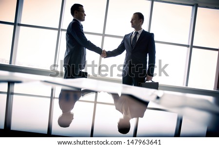 Silhouettes of two businessmen standing by the window and handshaking