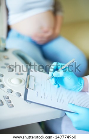 Gloved hand of obstetrician making notes during regular examination at hospital