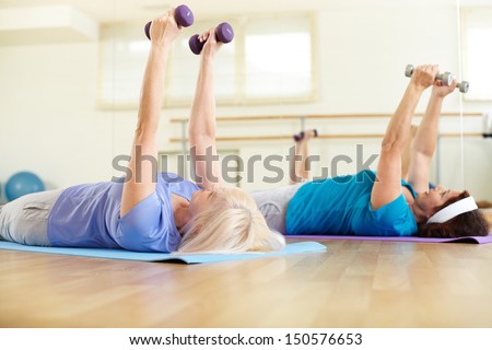 Image of two mature females doing exercise with barbells in sport club Image of two mature females doing exercise with barbells in sport club