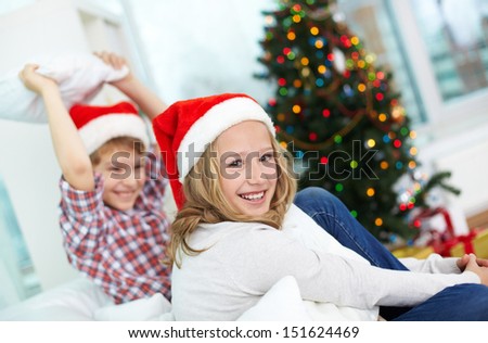 Portrait of happy girl looking at camera with her brother on background on Christmas evening
