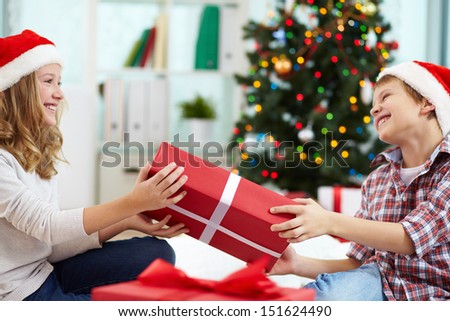 Portrait of happy siblings holding giftbox and looking at one another on Christmas evening