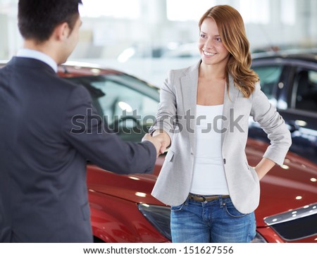 Image of car dealer handshaking with happy female in automobile center