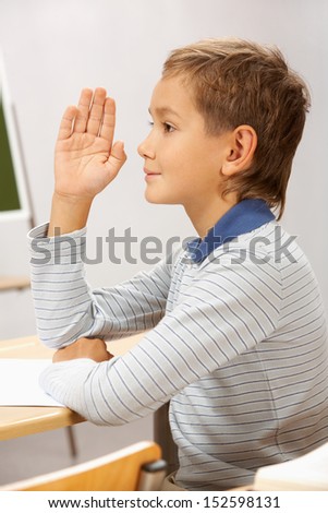 Portrait of smart lad at his place raising hand to answer during lesson