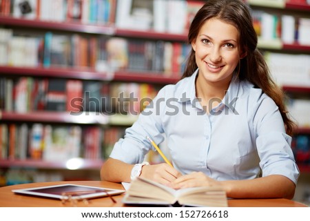 Portrait of pretty student looking at camera while working in college library