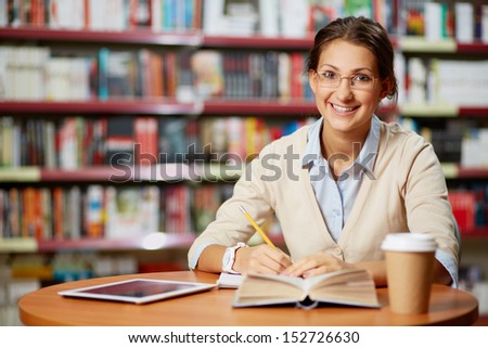 Portrait of clever student looking at camera and smiling in college library