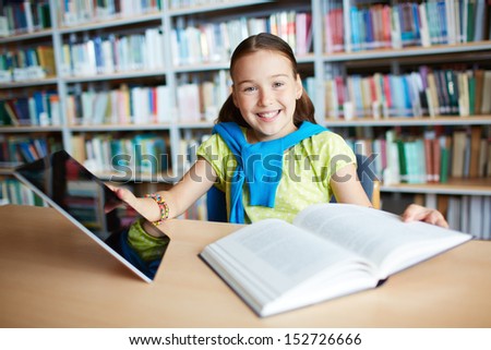 Portrait of a lovely girl with touchpad and open book sitting in library