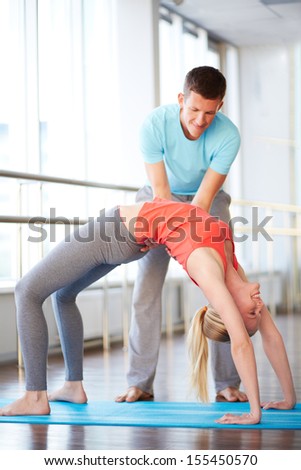 Portrait of young woman doing physical exercise with help of her trainer