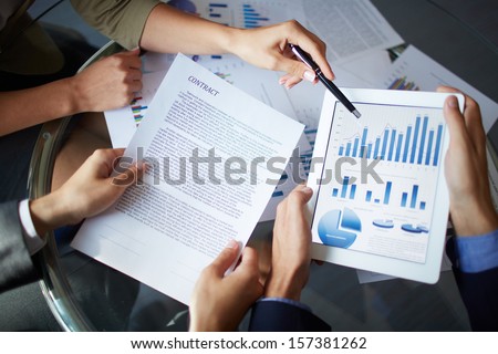 Image of human hands during discussion of paper and electronic documents at meeting