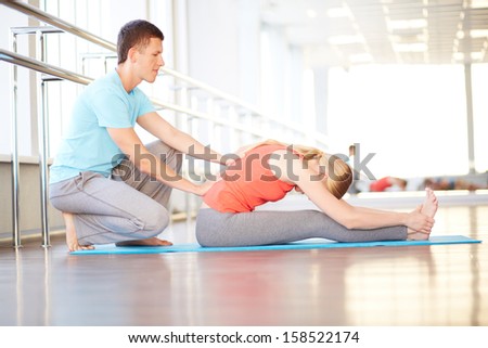 Portrait of young woman doing physical exercise with help of her trainer