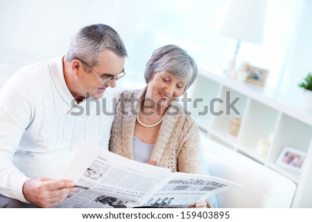 Portrait of happy mature couple sitting at home and reading newspaper together