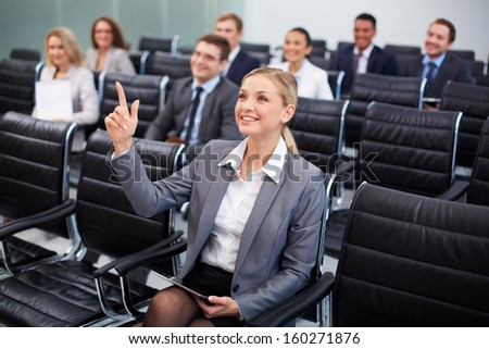 Image of business people sitting in rows at seminar with pretty woman in front raising her arm