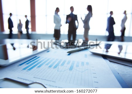 Close-Up Of Business Document In Clipboard At Workplace On Background Of Office Workers Interacting