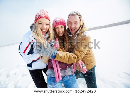 Portrait of happy friends standing in snowdrift in winter and laughing