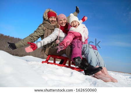 Happy couple and their daughter sitting on sledge Happy couple and their daughter sitting on sledge