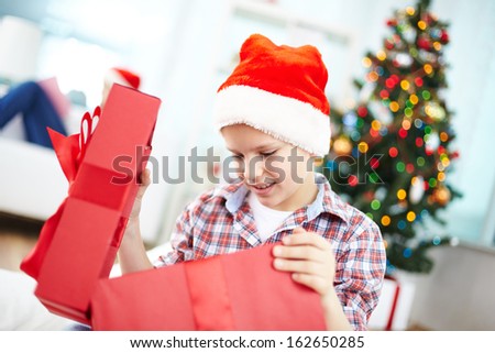 Portrait of curious boy looking inside big red giftbox on Christmas evening