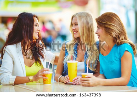Portrait of three happy girls chatting while having drink after shopping