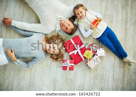 Happy family with giftboxes lying on the floor and looking at camera