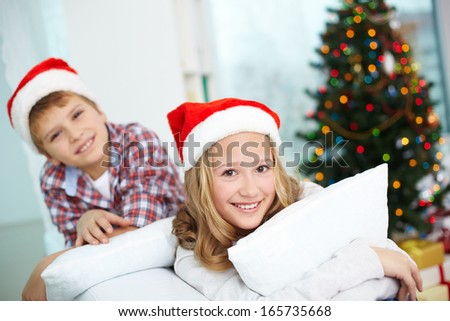 Portrait of happy girl looking at camera with her brother on background on Christmas evening