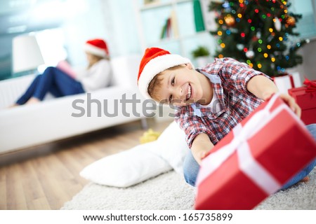 Portrait of cheerful boy giving red giftbox and looking at camera on Christmas evening