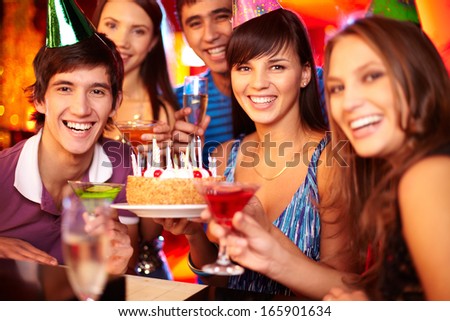 Portrait of joyful friends toasting and looking at camera at party with focus on happy girl and guy