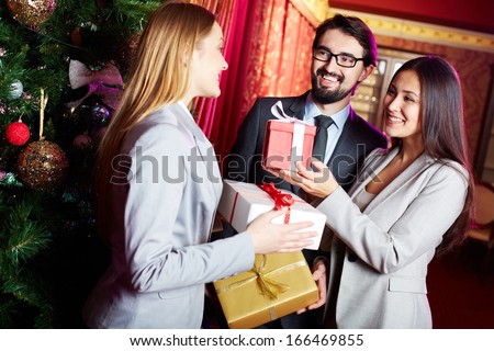 Portrait of joyful colleagues giving xmas presents to each other with xmas tree near by