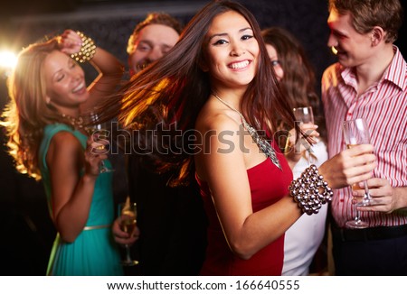 Portrait Of Cheerful Girl With Champagne Flute Dancing At Party While Smiling At Camera