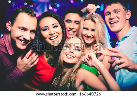 Portrait of happy girls and guys in smart clothes looking at camera at party
