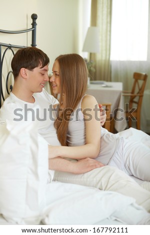 Pretty female and her husband looking passionately at one another in bed