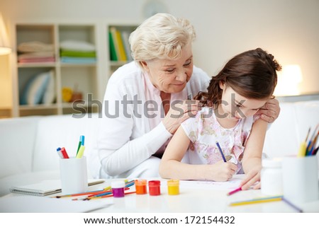 Portrait of cute girl making card for her mom with her grandmother near by