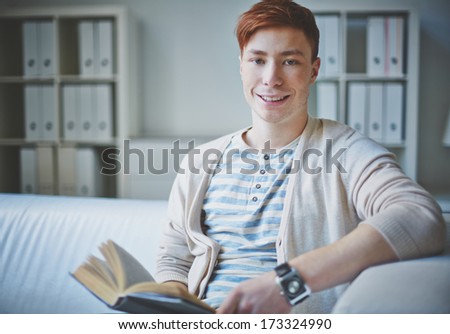 Portrait of young guy in casual clothes with open book looking at camera