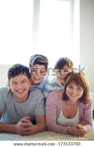 Portrait of happy family of four lying on the floor and looking at camera with smiles