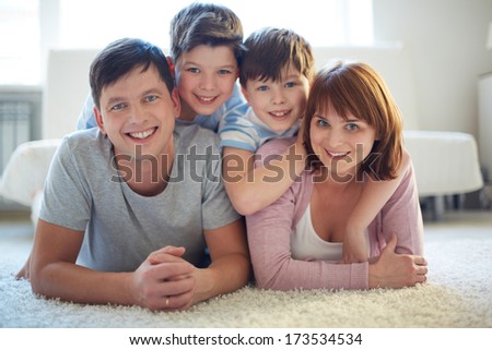 Portrait of happy family of four lying on the floor and looking at camera with smiles