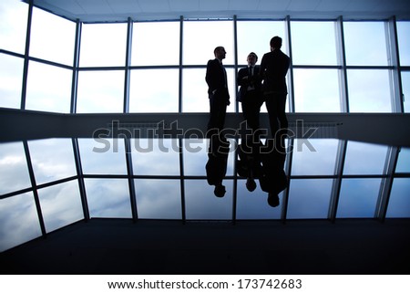 Group of colleagues standing against window in office and speaking