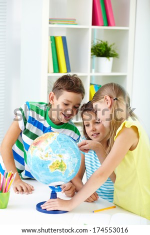 Portrait of curious classmates at workplace studying globe in classroom