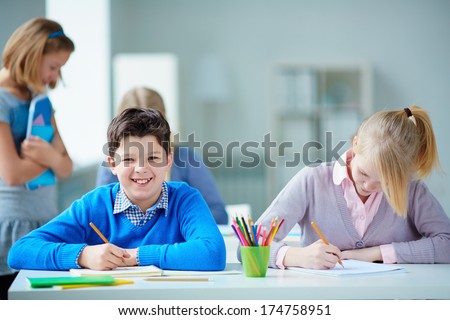 Portrait of happy schoolboy at workplace looking at camera on drawing lesson