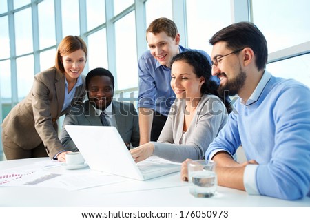 Group of business partners looking with smiles at laptop display at meeting