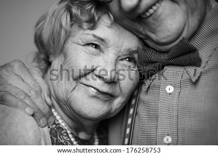 Black-and-white image of senior female being embraced by her husband
