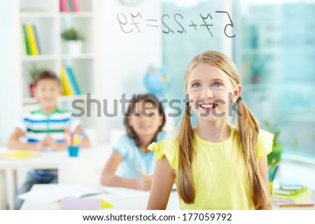Portrait of lovely girl looking at sums on transparent board with schoolmates on background