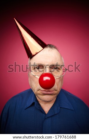 Portrait of unhappy man with a red nose and in a cone cap on fools day