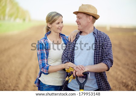 Image of two happy farmers looking at one another on background of plowed field