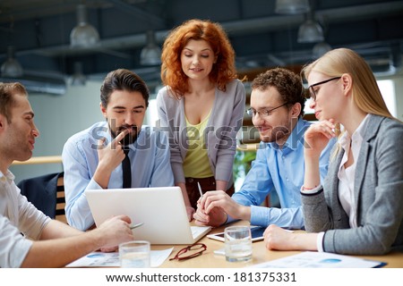 Group of business partners looking attentively at data in laptop at meeting