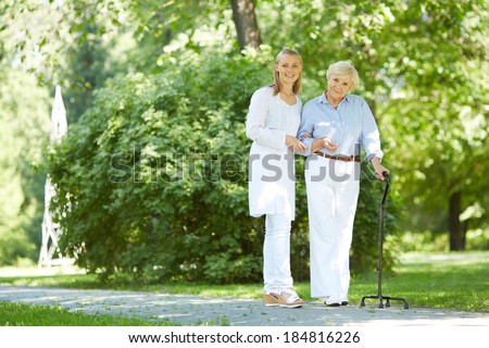 Pretty nurse and senior patient with walking stick having a walk in park