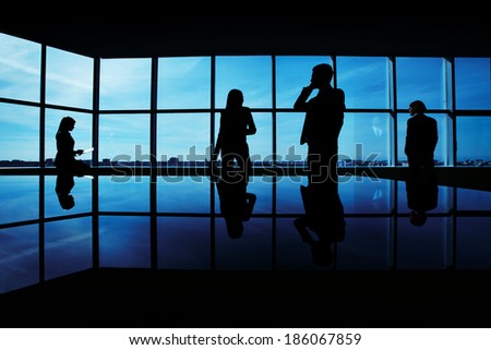 Silhouettes of several office workers working on background of window