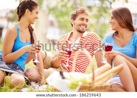 Happy young friends drinking red wine at picnic in the country