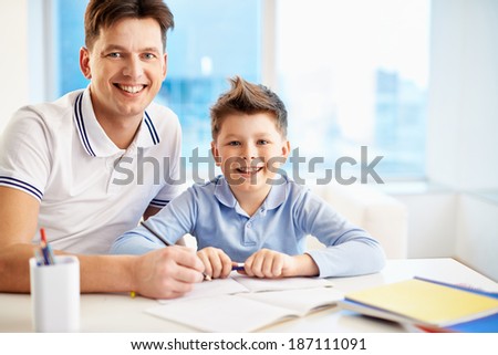 Photo of happy man and his son sitting by table and looking at camera