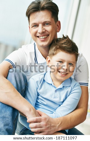 Photo of happy man embracing his son and both looking at camera