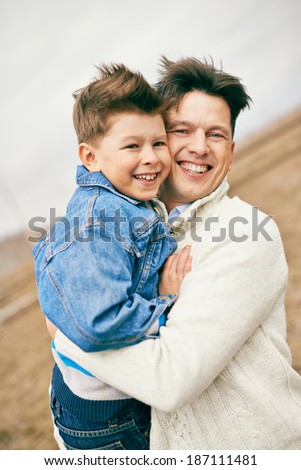 Photo of happy man embracing his son and looking at camera