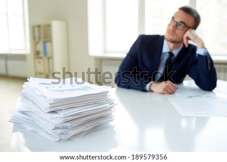 Stack of documents on the desk and pensive male employee working on background